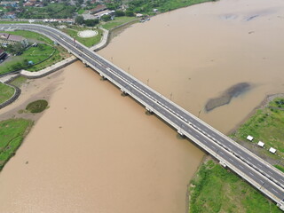 Aerial photograph showing a highway bridge spanning a wide river, surrounded by lush green...