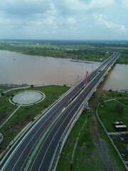 Aerial photograph showing a highway bridge spanning a wide river, surrounded by lush green...