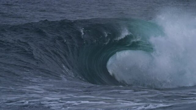 slow motion Atlantic wave rolls and crashes into a smooth barrel on a stormy day