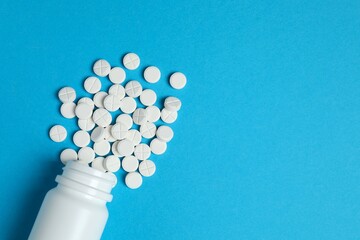 White pills pouring out of a medicine bottle on a color background