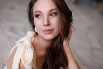 A beautiful girl in a short elegant beige gold dress stands on the sand. Portrait of a beautiful woman on a gray background. Bright make-up and long hair. Gorgeous brunette woman portrait