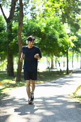 Active young man listening to music jogging on a sunny park pathway