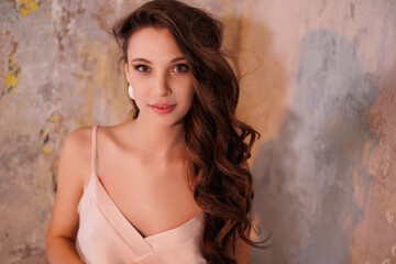 Fototapeta premium A beautiful slender tall brunette in a silk beige dress. A magnificent portrait of a gorgeous girl with long hair down, stand on sand