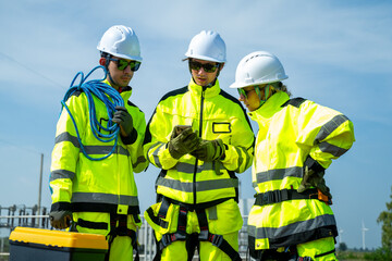An engineer wearing safety gear closely inspects the base of a wind turbine in a renewable energy field.