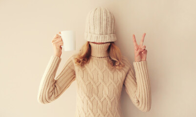 Happy funny young woman with cup of coffee drink in winter hat, sweater having fun on background