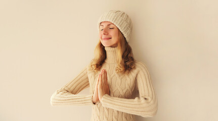 Portrait of relaxed young woman meditates in yoga position closed eyes winter sweater and hat