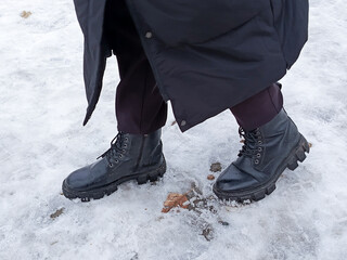 Feet in warm, black boots on the snow. A man in a black, long down jacket walks through the snow in winter. Winter clothes. Frost in the city.