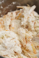 A close-up view of a mixture of flour and orange zest in a metal bowl, being mixed together with a spoon.