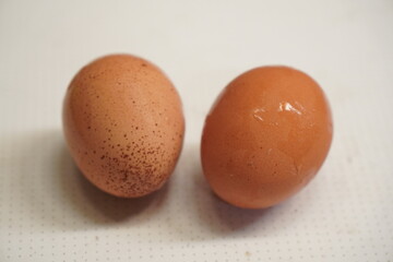 Two brown eggs on a white surface, one with a more textured shell and the other with a smoother one.