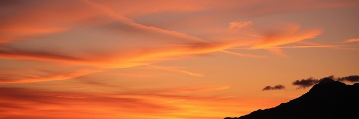 Fototapeta premium The silhouette of a mountain peak against a vibrant sunset with clouds drifting across the horizon, serene, sunsets, peaceful