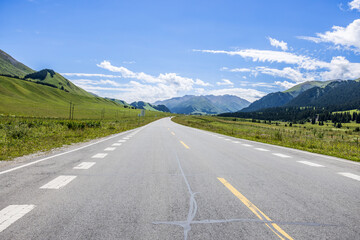 Fototapeta premium Countryside asphalt road and green meadow with mountains nature landscape on a sunny day. Road trip.