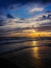 Colorful beach sunset with deep sky and clouds, sun rails over the sea waves