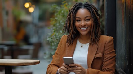 Happy woman with dreadlocks smiles while using her smartphone outdoors at a cafe.