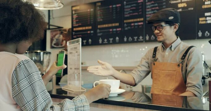 Young girls using e-payment with mobile to buy hot drink in coffeeshop