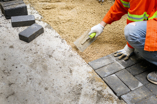 Worker laying brick pavers on the sidewalk.  Road paving and repairing project.