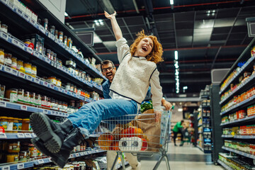 Cheerful couple having fun riding shopping cart in supermarket