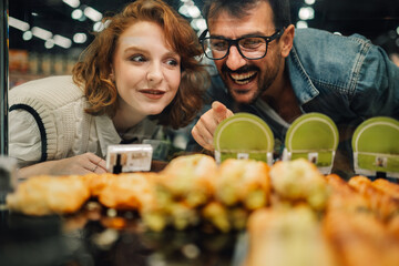 Happy couple choosing pastries in supermarket bakery display