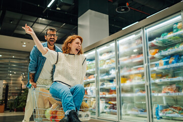 Happy couple having fun riding shopping cart in supermarket