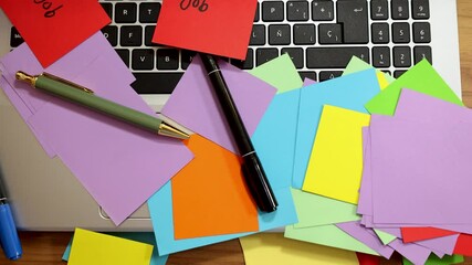 Slow motion zoom of colored paper stickers on laptop with pencils, pens on it and red notes that say job