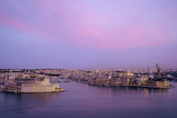 View of the Grand Harbour in Senglea, Malta, with historical fortifications at sunset, soft pink hues in the sky.