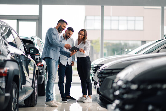 Customers closely inspecting sleek car with tablet support.