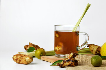 Hot red ginger drink in a glass cup with some raw ginger and lemon