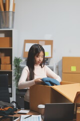 Startup SME small business entrepreneur of freelance Asian woman wearing apron using laptop and box to receive and review orders online to prepare to pack sell to customers, online sme business ideas.