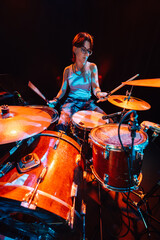 Female drummer performing energetically on stage with drum kit