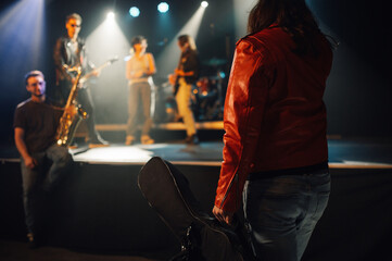 Roadie carrying guitar case walking towards stage with band performing