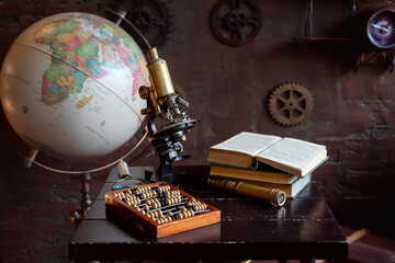 Vintage objects with a globe, microscope, and abacus on a wooden desk, symbolizing science and...