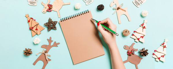 Top view of female hand making some notes in noteebok on blue background. New Year decorations and toys. Christmas time concept