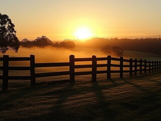 Obraz premium Sunrise Serenity A Peaceful Pastoral Scene of Golden Hour Light Illuminating a Misty Field, Encapsulating the Tranquil Beauty of Rural Life The Rising Sun casts Long Shadows Across a Wooden Fence