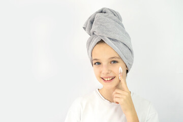 Beautiful girl with a towel on her head smearing her face with cream. facial skin care, skin problems in teenagers. Moistening