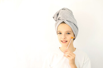 Beautiful teenage girl with towel on her head smiling and taking care of her facial skin with a brush. Skin care for a teenager. White background, space for text