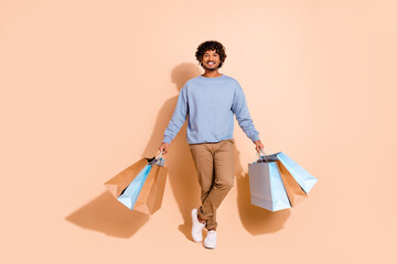 Full body photo of positive cheerful guy wear blue shirt trousers holding shopping bags in hands...