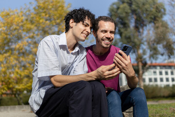 Gay couple smiling and using mobile phone outdoors