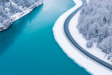 Aerial view of a snowy road running alongside a turquoise river surrounded by frosted trees