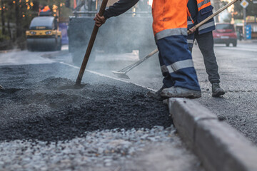 Road construction worker leveling asphalt with a shovel. Focus on foreground