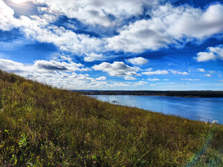 Tranquil lakeside view with grassy hillside under a clear blue sky in the afternoon