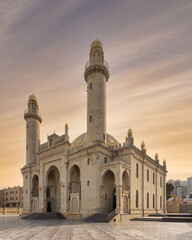 The majestic Taza Pir Mosque in Baku, Azerbaijan is captured in a sunset shot. The mosque features intricate architecture and twin minarets. The scene is set against a peaceful early evening sky