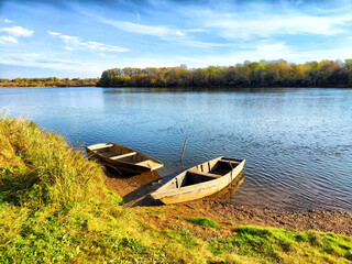 Obraz premium Two wooden boats resting on the shore of a tranquil river surrounded by lush trees on a sunny day