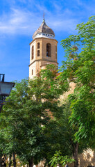 Obraz premium A tall tower with a cross on top stands in front of a green tree. Sacred Chapel of the Savior in Ubeda, Spain
