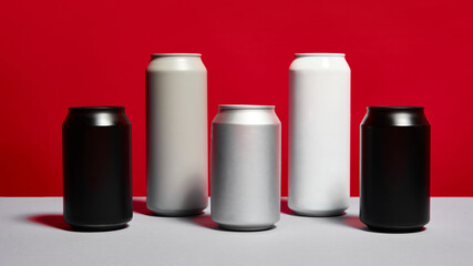 Five aluminum beverage cans in different colors, and sizes, arranged in row on gray surface against red background. Mockup and advertisement for various drink types like soda, beer, energy drinks