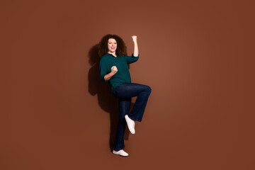 Full length photo of cheerful lucky lady dressed green shirt rising fists empty space isolated brown color background