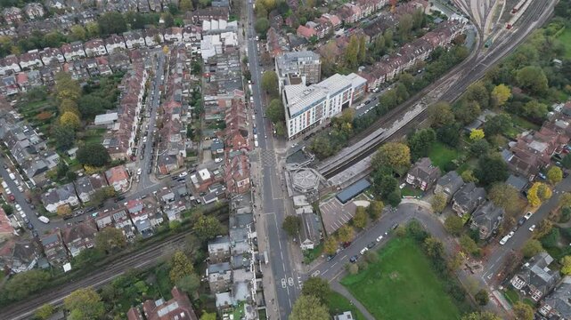 Pan-down aerial view of Ealing Common Underground Station, with surrounding British residential architecture, green spaces, and intricate roadways, Ealing, London, UK