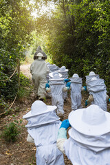 Children in beekeeping suits following their teacher on a dirt path through the forest