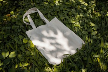 White tote bag on vibrant green grass under soft dappled sunlight with crinkled fabric texture and gentle shadows creating a natural and elegant composition