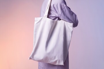 Blank white tote bag slung over shoulder with smooth pastel gradient background transitioning from peach to lavender and natural lighting highlighting texture