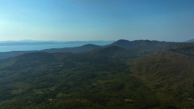 Caha Pass, County Cork, Ireland, September 2024. Drone high angle aerial descent facing south with panoramic overview of the rugged green landscape with haze out to the North Atlantic ocean.