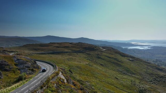 Caha Pass, County Cork, Ireland, September 2024. Drone pushes forward above a winding road with cars exploring the scenic landscape with Glengarriff and the North Atlantic Ocean in the background.